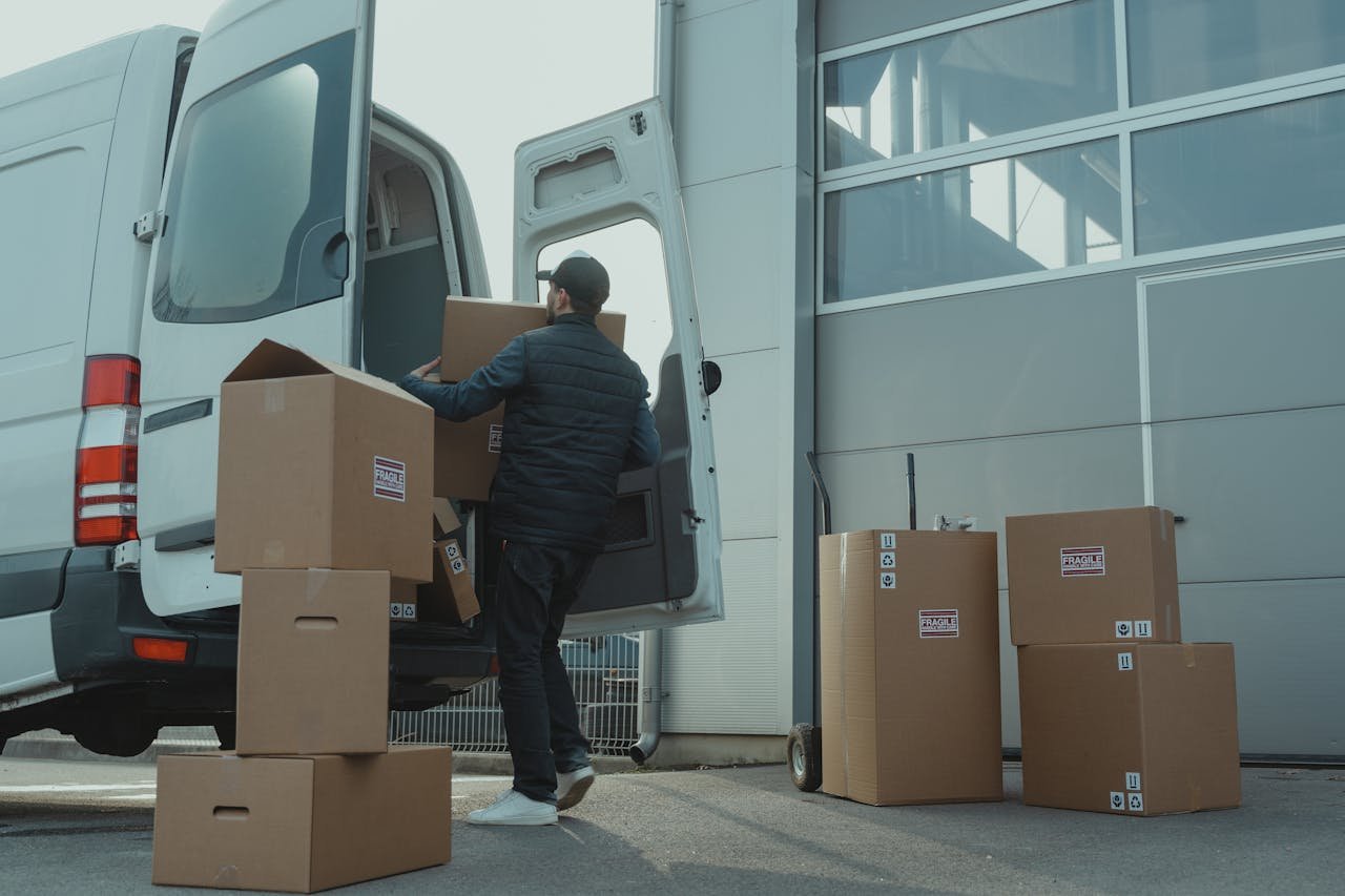 Services A delivery man unloading cardboard boxes from a van at a warehouse during the day.